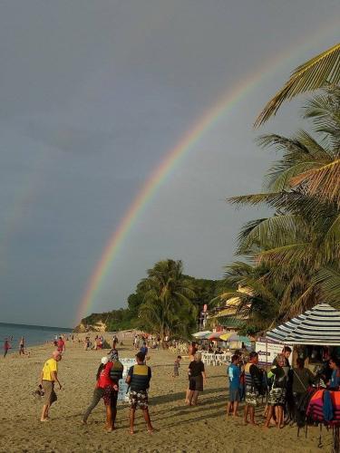 regenboog boven strand vol mensen, rechts palmbomen