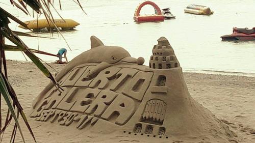 Letters in een zandsculptuur: Puerto Galera, op de achtergrond vlakke zee met opblaasboten en bananaboten